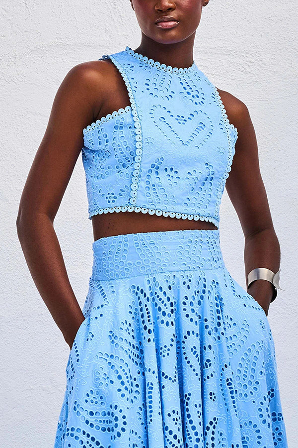 Close-up of a model in a blue embroidered top and high-waist maxi skirt against a white wall.