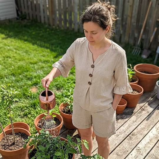 Woman in beige casual set watering plants on a wooden deck.
