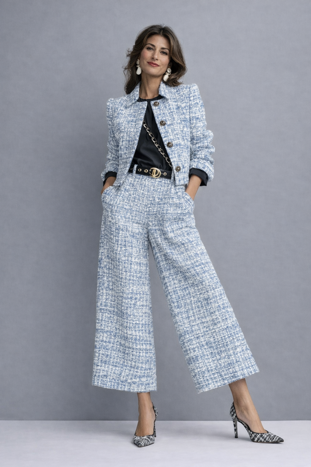Woman wearing a blue and white patterned pantsuit, hands in pockets, posed against a gray studio backdrop.
