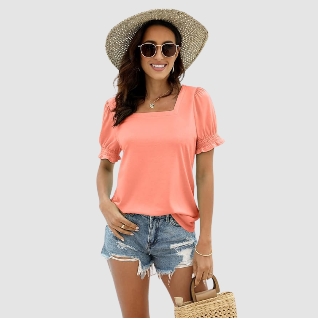 Woman styled in peach square neck top, distressed denim shorts, straw hat, carrying woven handbag in a studio shot.