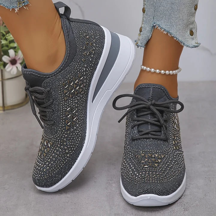 Gray orthopedic sneakers featuring subtle shine, worn with jeans in a bright indoor setting.