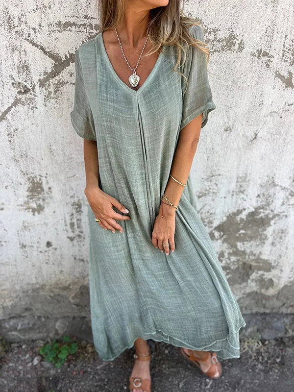 Green V-neck dress with short sleeves, worn by a person in front of a textured wall.
