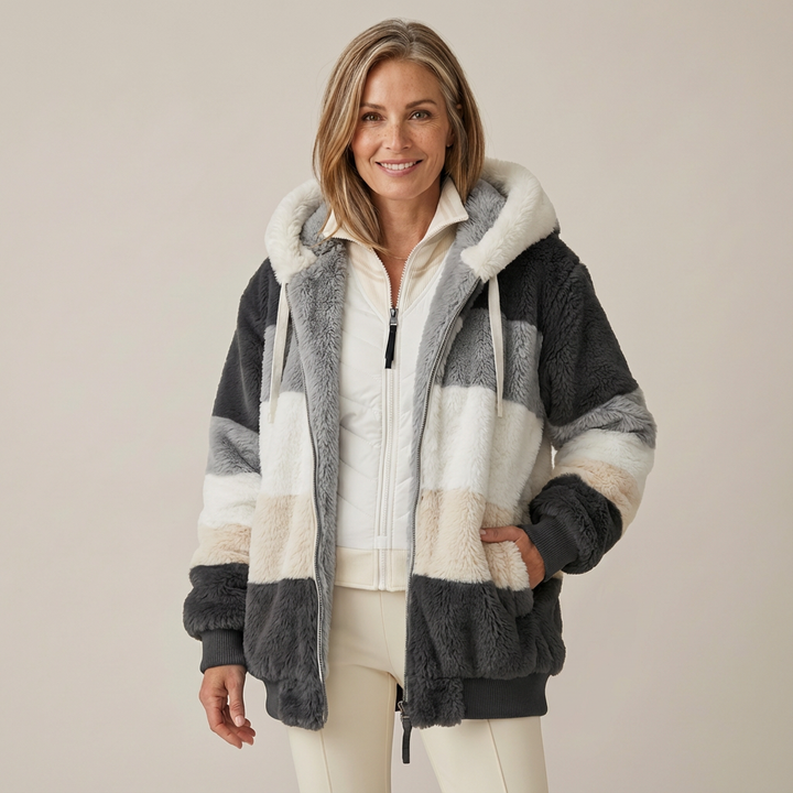Woman wearing a plush, multicolored hooded jacket in white, gray, and beige stripes, in a studio setting.