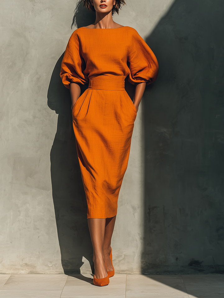 Elegant orange skirt set with puff sleeves in studio setting against a textured wall.