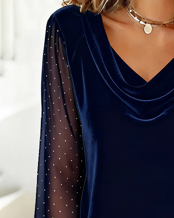 Close-up of navy blue blouse with draped collar and sheer polka dot sleeve in an indoor environment.