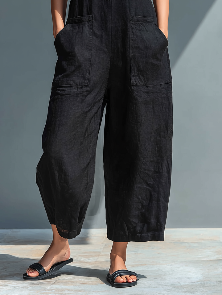 Close-up of the bottom half of a black sleeveless jumpsuit with pockets, worn by a woman outdoors.