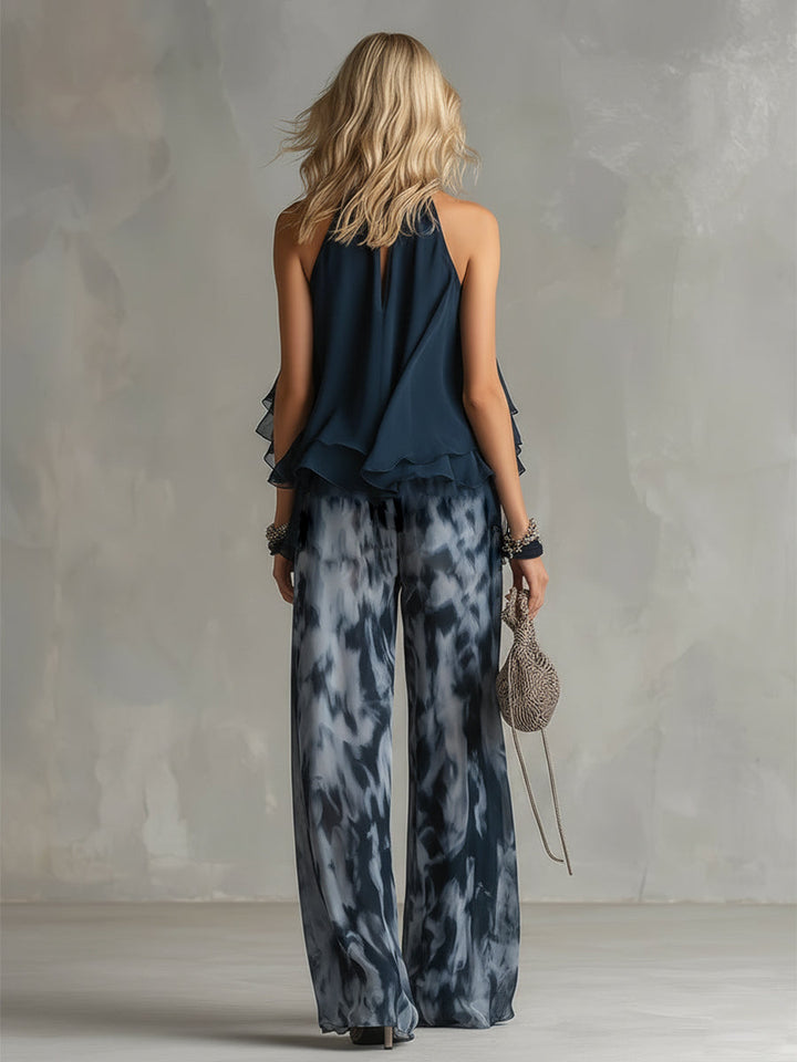 Back view of an elegant halter neck top with flowing layers and wide-leg patterned pants. Studio setting.