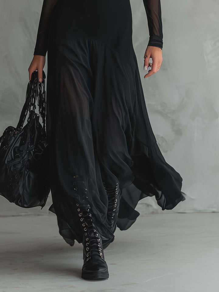 Close-up of flowing black maxi dress skirt with sheer detailing, paired with black lace-up boots, on a gray indoor floor.