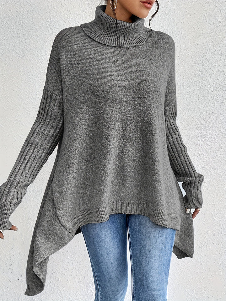 Gray turtleneck sweater with ribbed sleeves, worn with jeans, in front of a plain white wall.
