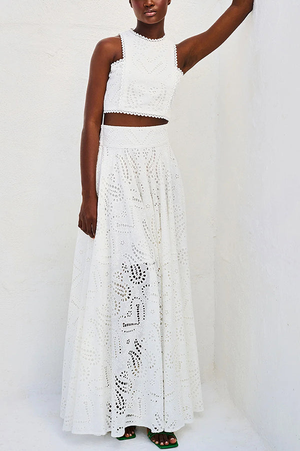 Woman in a white embroidered top and high-waist maxi skirt leaning against a wall with a serene backdrop.