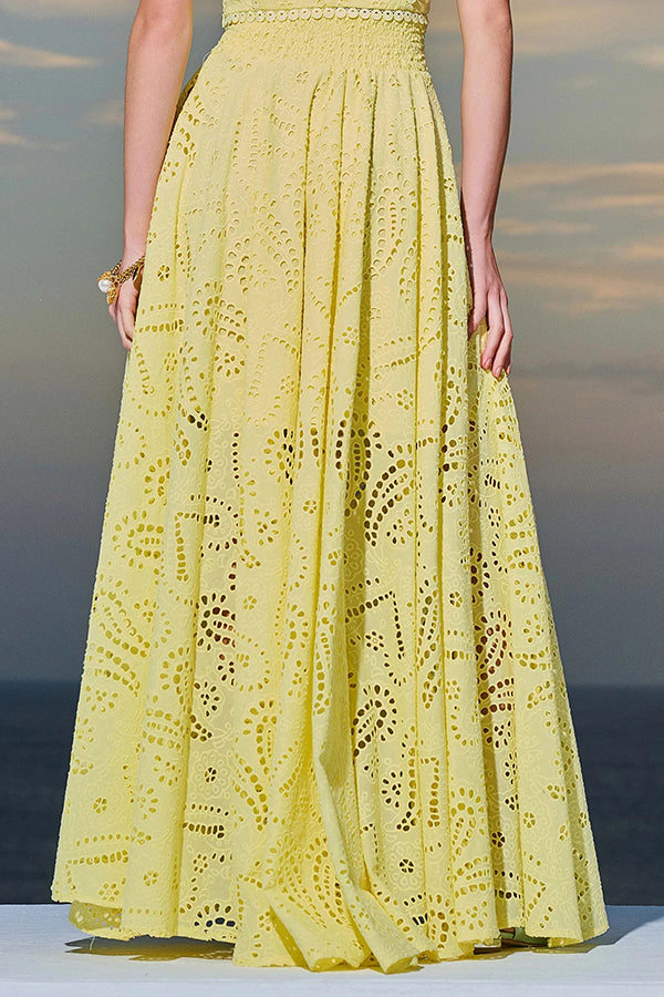 Model in a yellow embroidered high-waist maxi skirt against a scenic ocean view at sunset.