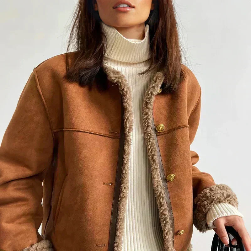 Woman in a brown jacket with soft trim, white turtleneck, and holding a bag, in a well-lit indoor space.