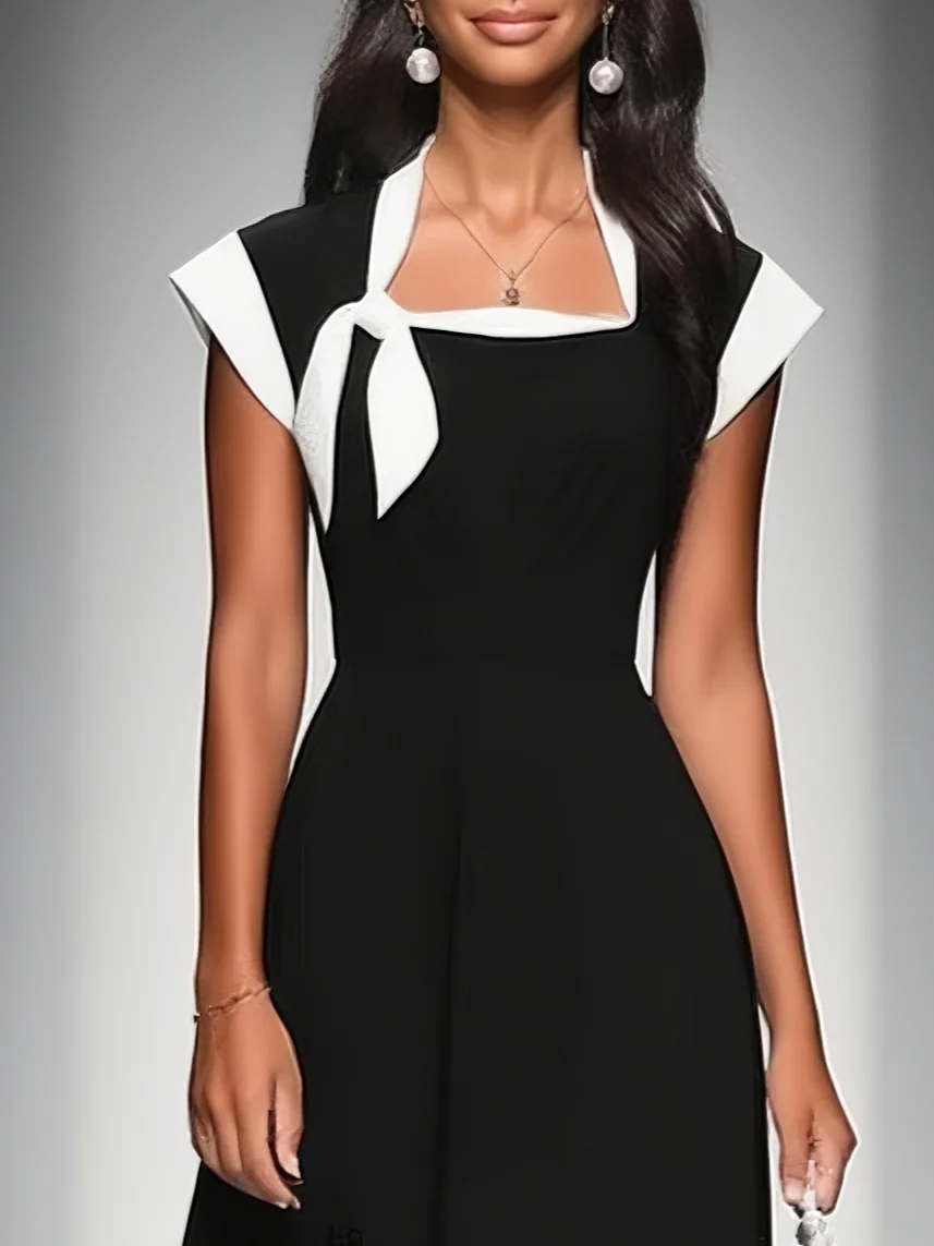 Close-up of black midi dress with white necktie detail, model wearing pearl earrings, studio background.