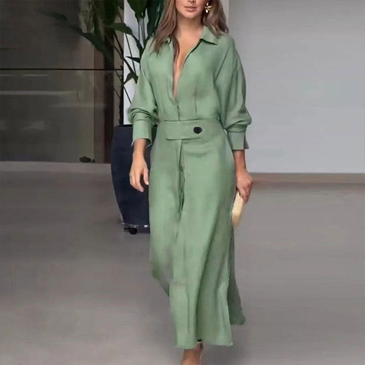 Woman in green midi dress with a deep V-neck and button detail walking in a modern indoor space with plants.