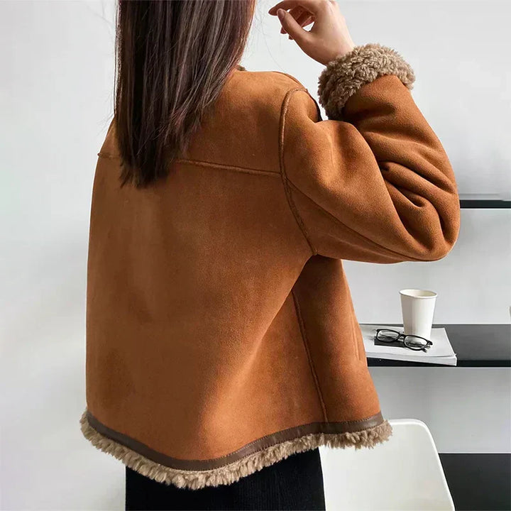 Back view of brown jacket with soft trim, worn by a woman indoors, near a table with a coffee cup and glasses.