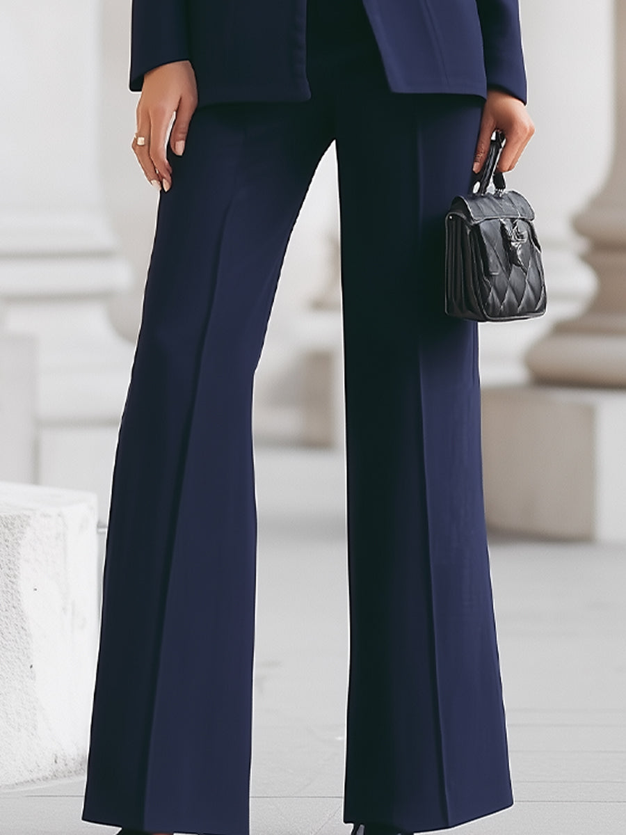 Close-up of navy trousers, part of elegant suit, worn outdoors with stone pillars, showcasing black quilted handbag.