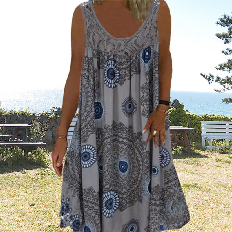 Woman in gray printed dress outdoors with sea and benches in background.