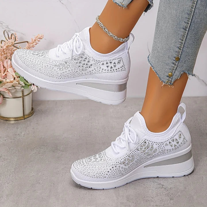 White orthopedic sneakers with glossy accents worn in a relaxed indoor setting, coupled with denim.