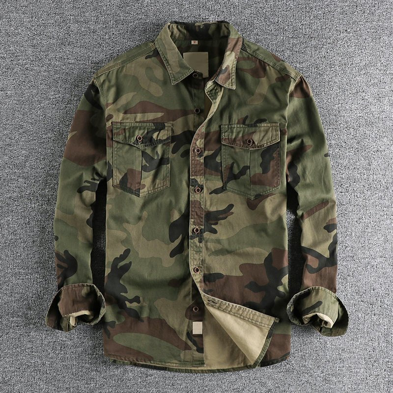 Green urban camo shirt with varied tones, laid on a gray textured backdrop, sleeves folded.