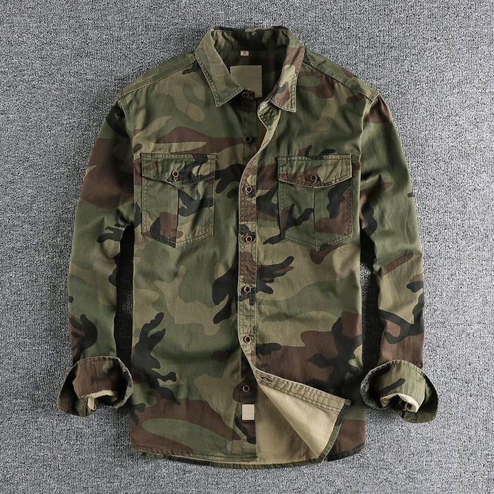 Green urban camo shirt with varied tones, laid on a gray textured backdrop, sleeves folded.