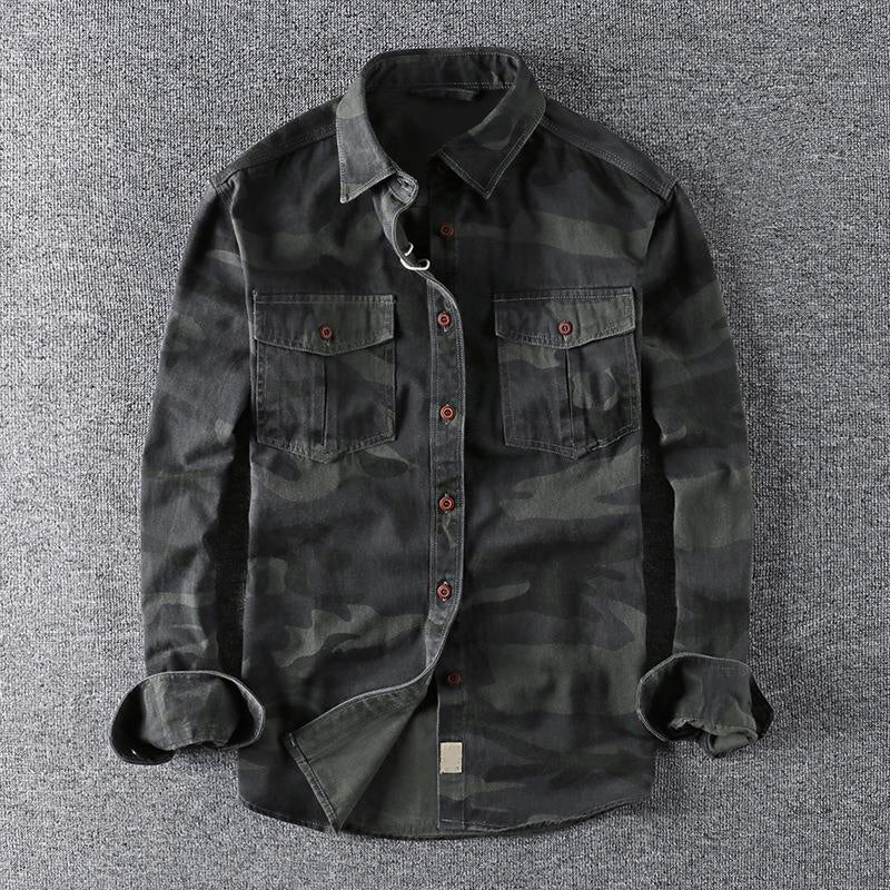 Dark urban camo shirt laid out on a gray surface, showcasing front pockets and folded sleeves.