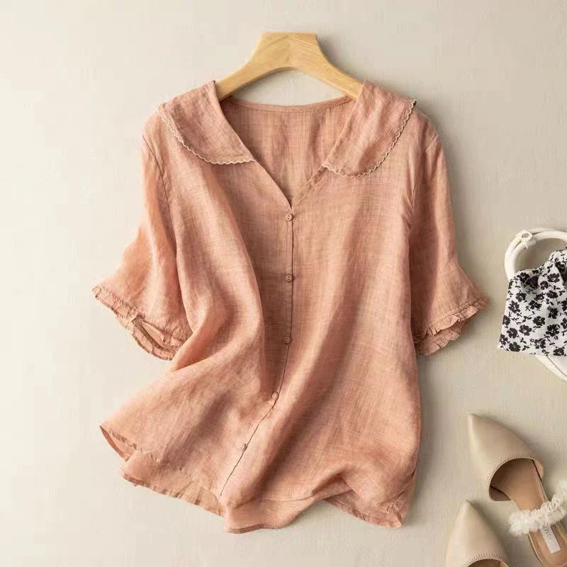 Peach short sleeve blouse with delicate trim on hanger, indoor background with shoes and handbag.