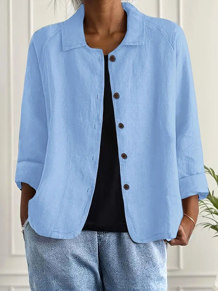 Light blue long sleeve top with button-down front, worn over a black shirt. Indoors, white paneled wall backdrop.