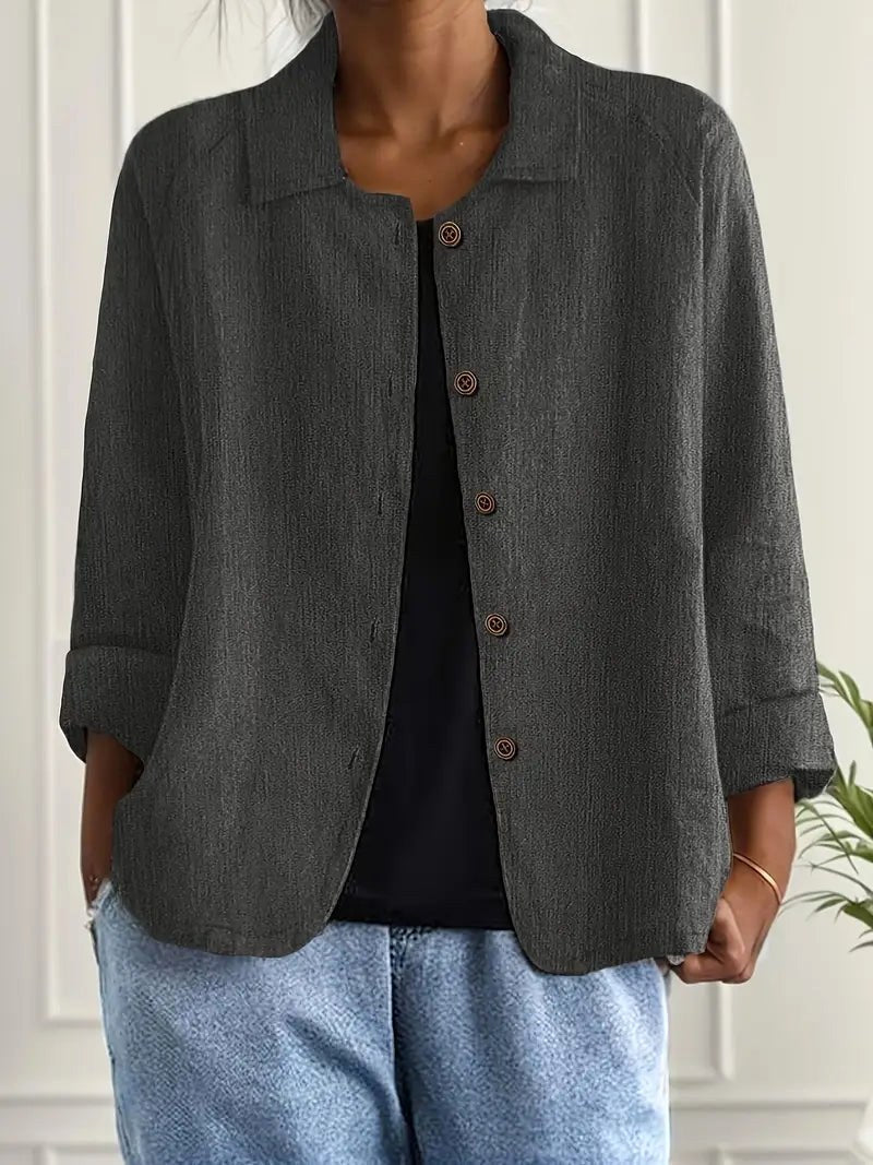 Charcoal gray long sleeve top with button-down front, worn over a black shirt. Indoors, white paneled wall backdrop.