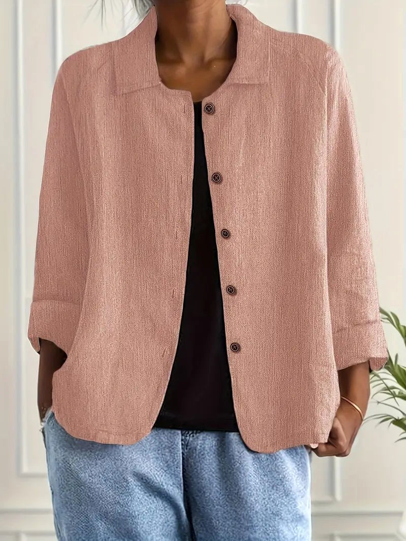 Light pink long sleeve top with button-down front, worn over a black shirt. Indoors, white paneled wall backdrop.