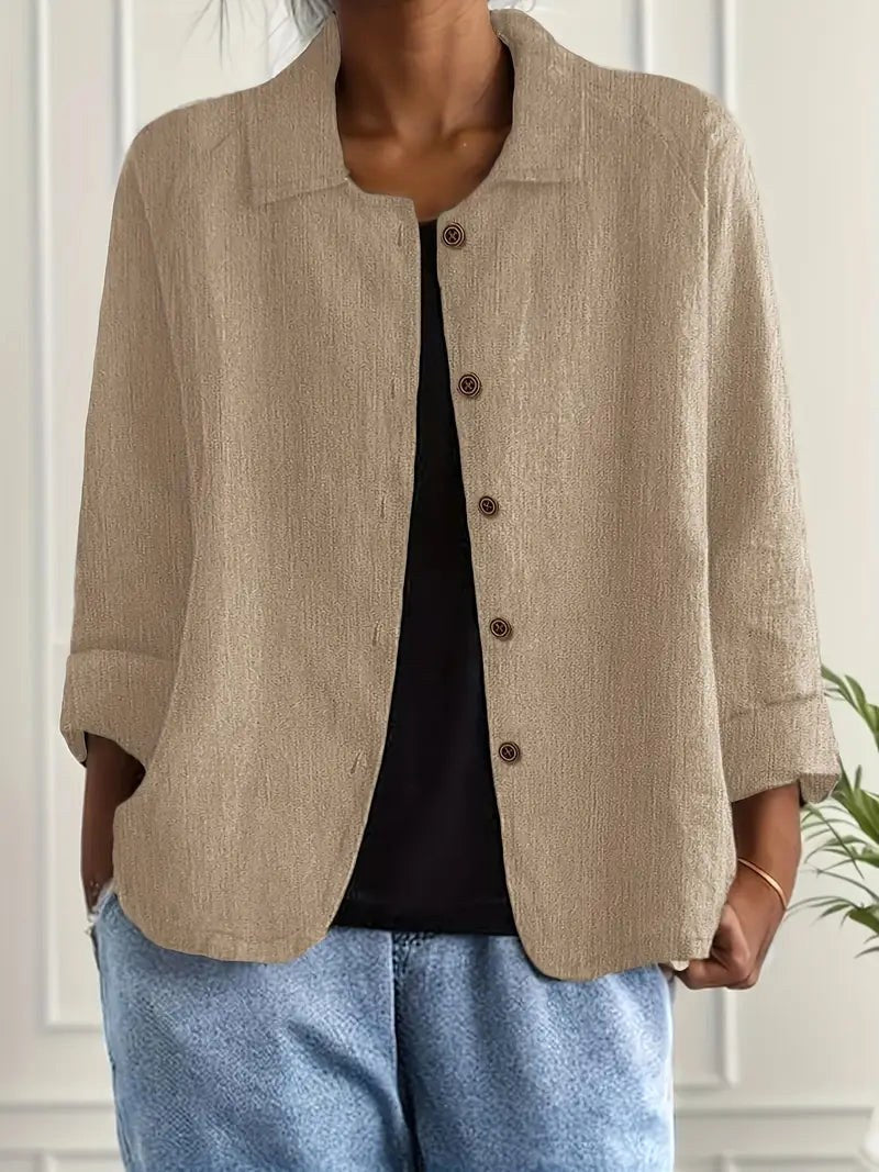 Beige long sleeve top with button-down front, worn over a black shirt. Indoors, white paneled wall backdrop.