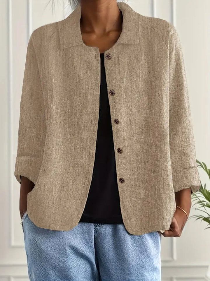 Beige long sleeve top with button-down front, worn over a black shirt. Indoors, white paneled wall backdrop.