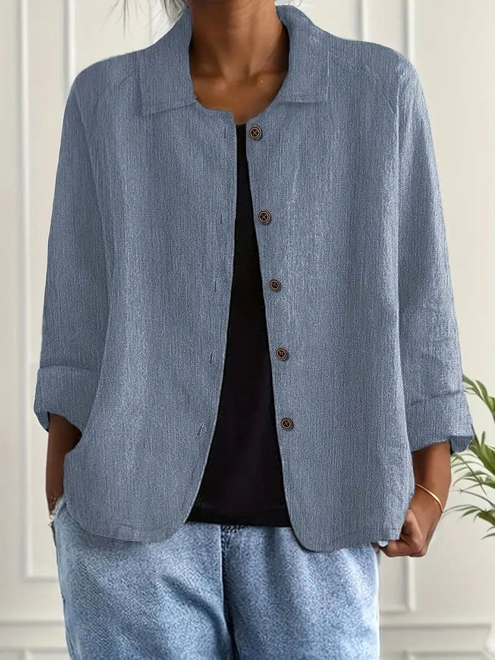 Gray-blue long sleeve top with button-down front, worn over a black shirt. Indoors, white paneled wall backdrop.
