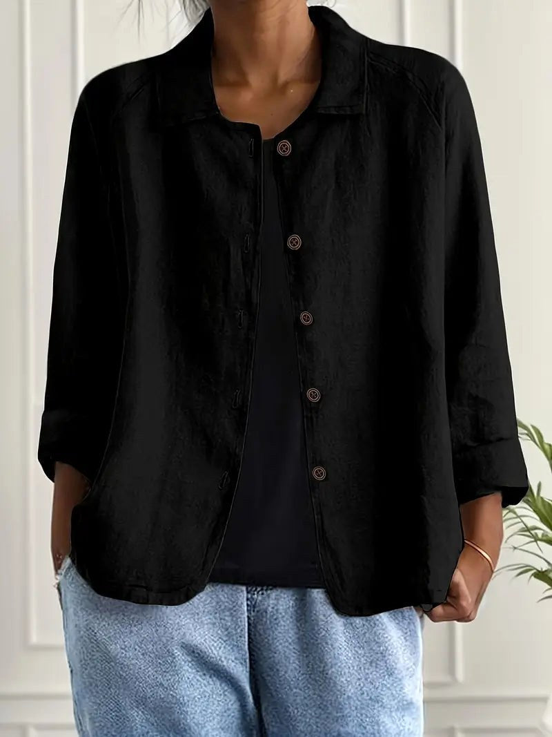 Black long sleeve top with button-down front, worn over a black shirt. Indoors, white paneled wall backdrop.