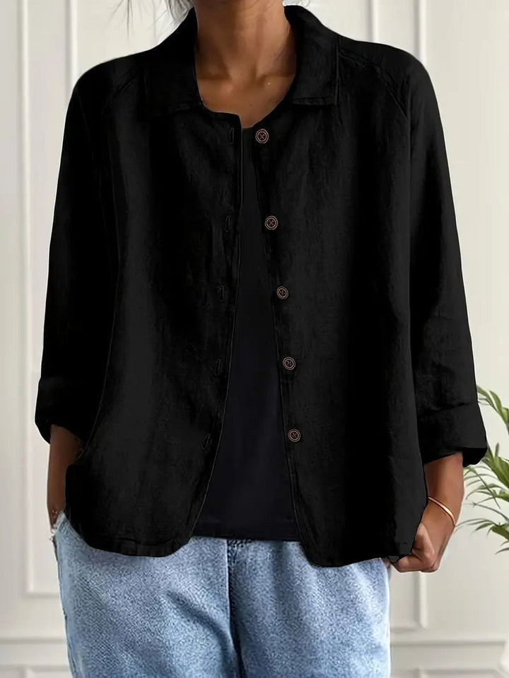 Black long sleeve top with button-down front, worn over a black shirt. Indoors, white paneled wall backdrop.
