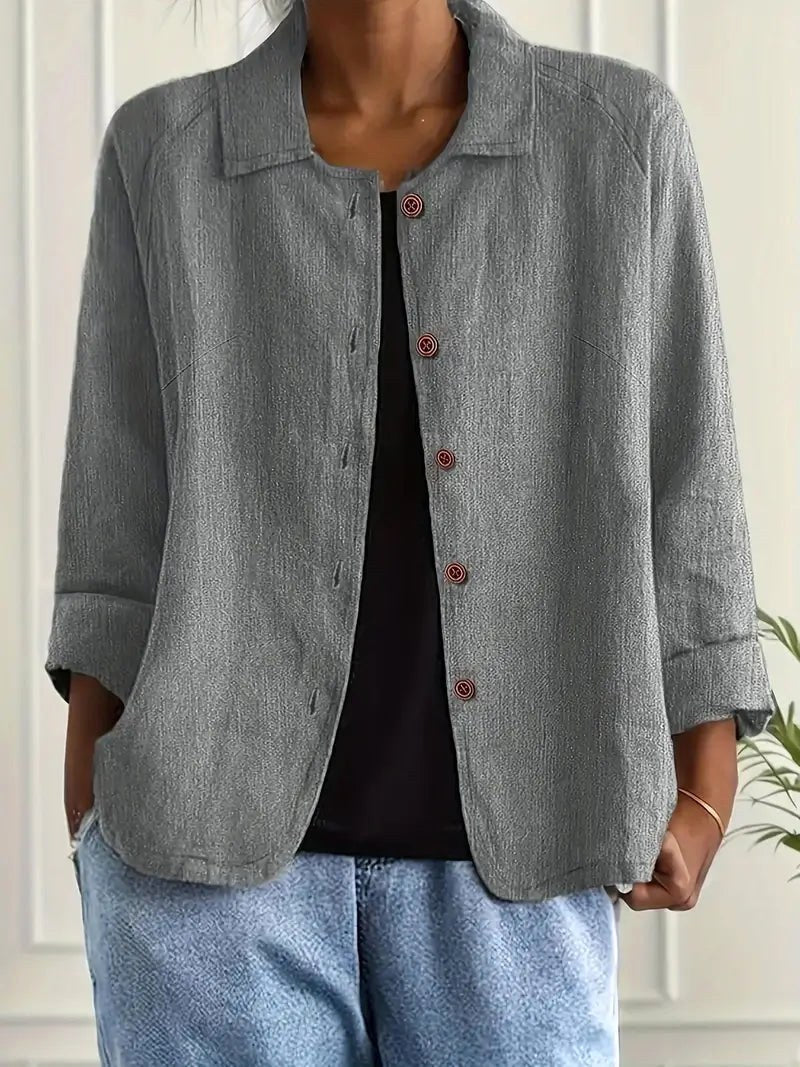 Light gray long sleeve top with button-down front, worn over a black shirt. Indoors, white paneled wall backdrop.