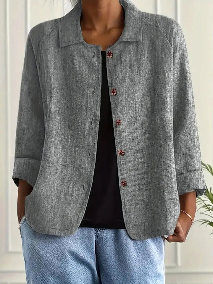 Light gray long sleeve top with button-down front, worn over a black shirt. Indoors, white paneled wall backdrop.