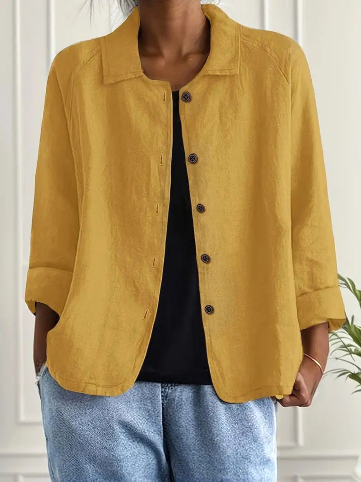 Yellow long sleeve top with button-down front, worn over a black shirt. Indoors, white paneled wall backdrop.