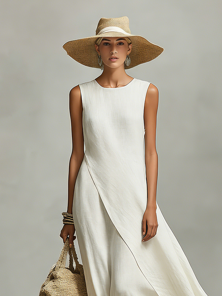 Woman in an ivory loose-fit maxi dress with a wide-brimmed hat, holding a woven bag, standing in a studio.