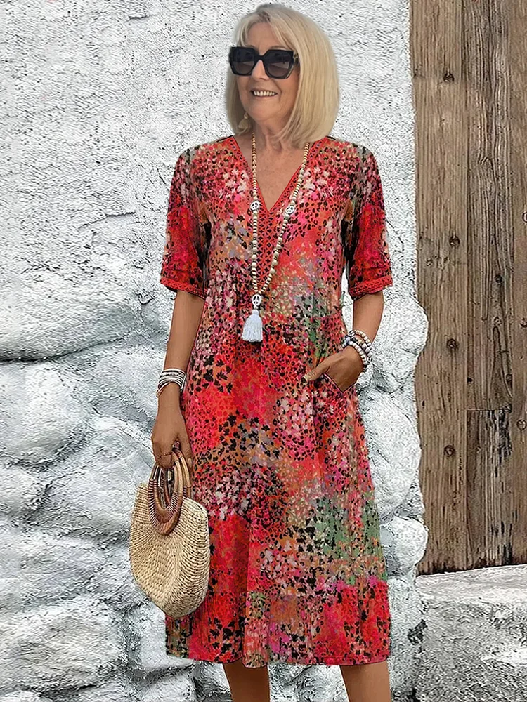 Lady in a vibrant red floral midi dress, accessorized with a straw bag, standing in front of a rustic textured wall.