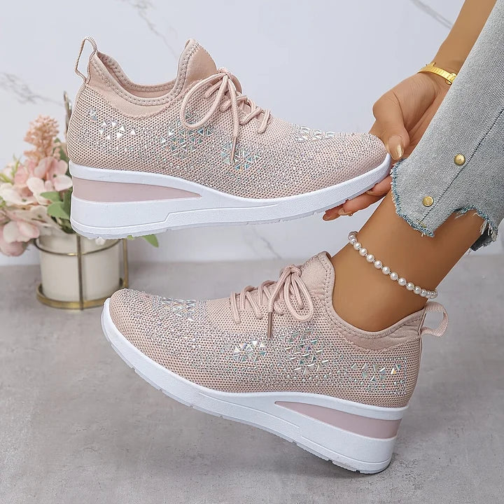 Soft pink orthopedic sneakers with delicate sparkle, worn with jeans against a neutral indoor space with flowers.