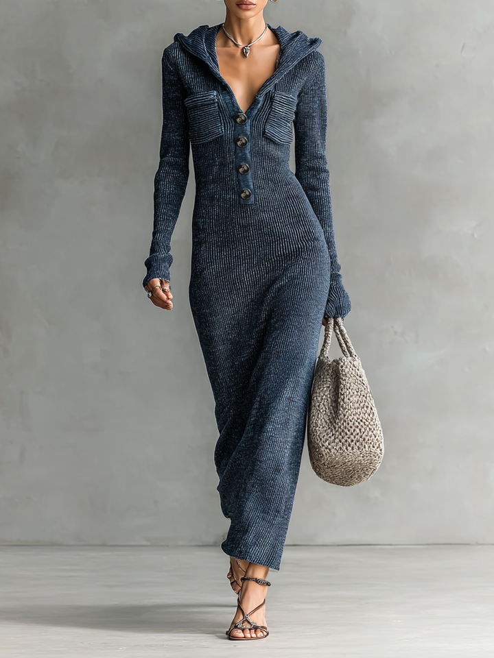 Woman wearing a dark blue slim-fit hooded maxi dress with button detail, standing against a neutral background holding a woven bag.