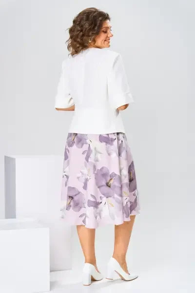 Back view of woman in a white top and pastel floral midi skirt in a white studio setting.