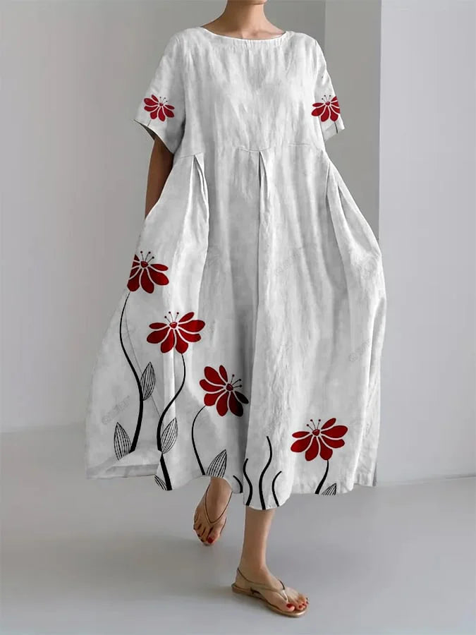Woman wearing a white floral summer dress with red flowers, standing in a minimalist indoor setting.