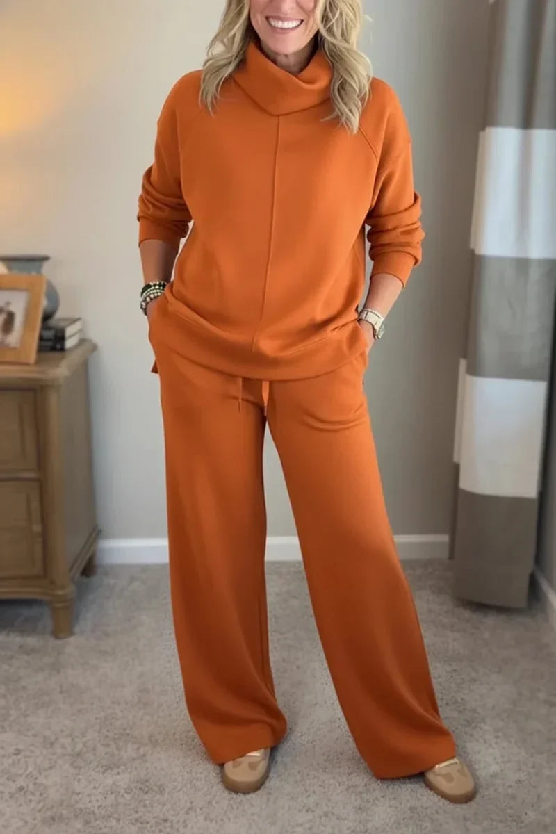 Woman wearing an orange comfortable set with long sleeves and wide-leg pants, standing in a cozy, carpeted room.