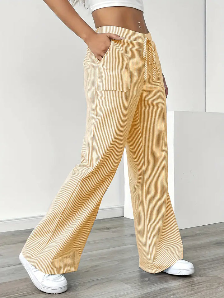 Side view of yellow and white striped pants with drawstring and pockets, modeled indoors with white sneakers.