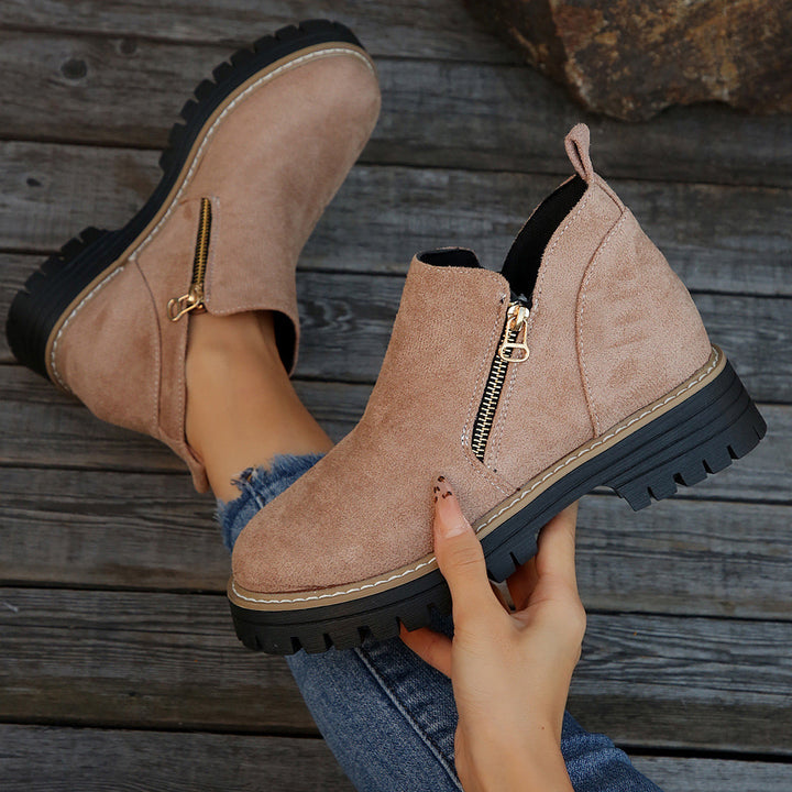 Taupe ankle boots with zipper, held in hand on a wooden surface with jeans.