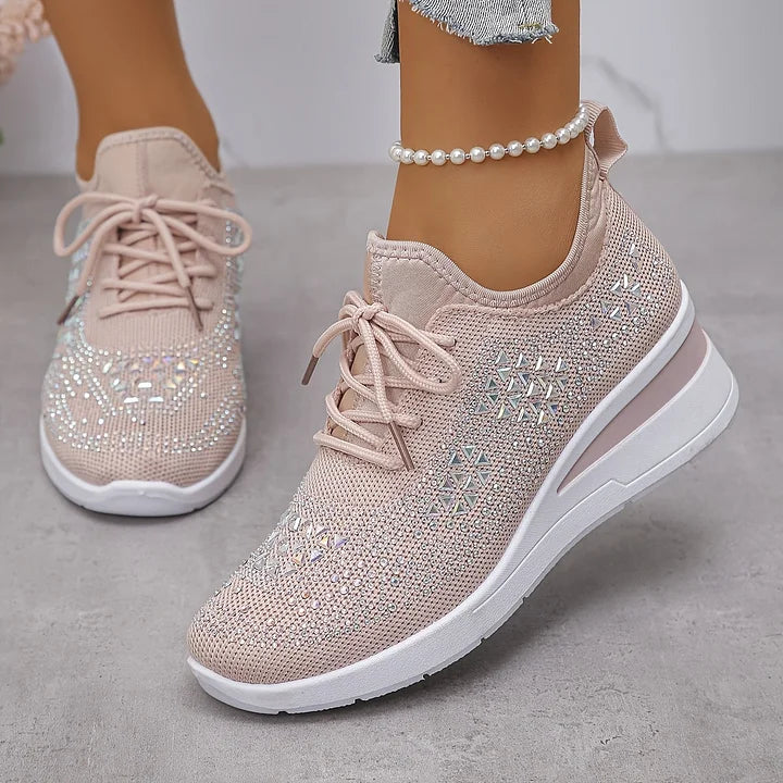 Front view of light pink orthopedic sneakers with subtle shine, paired with jeans in a neutral setting.