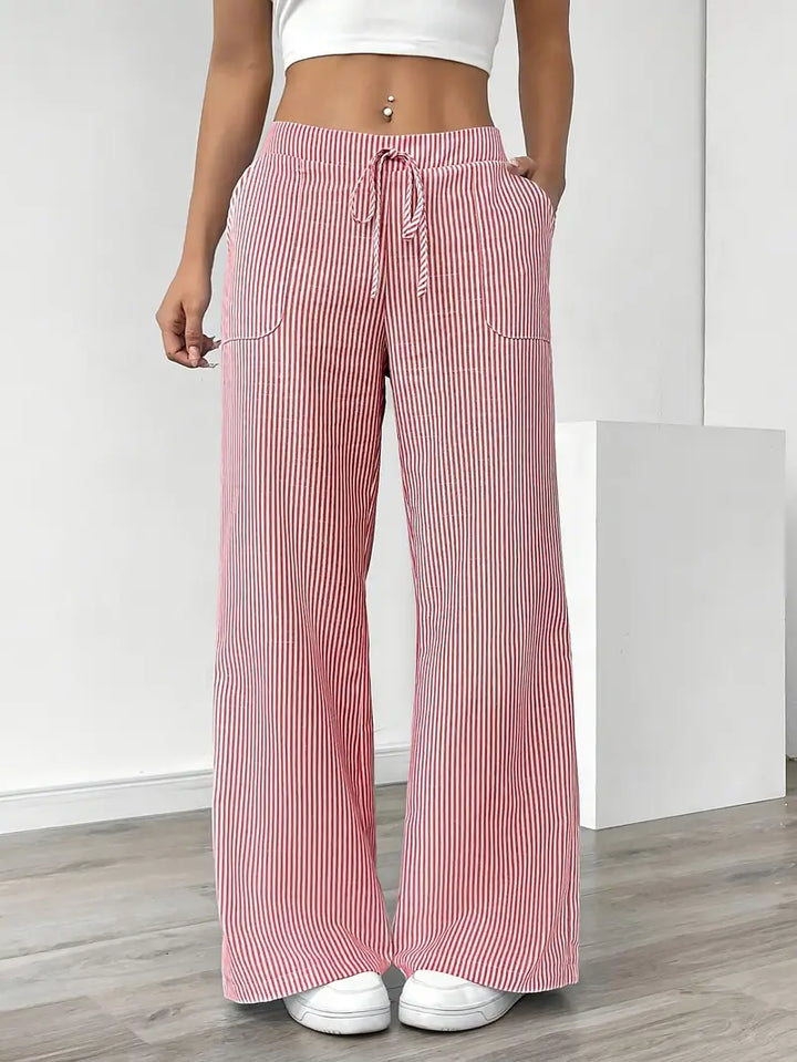 Red and white striped relaxed pants with drawstring waist, modeled indoors, paired with white sneakers and crop top.
