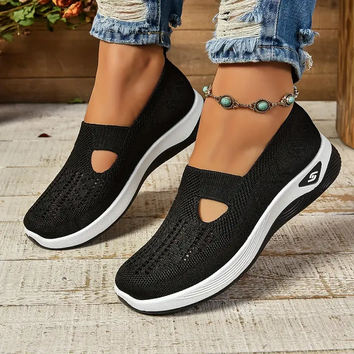 Black non-slip orthopedic shoes worn with anklet, distressed jeans on wooden floor.