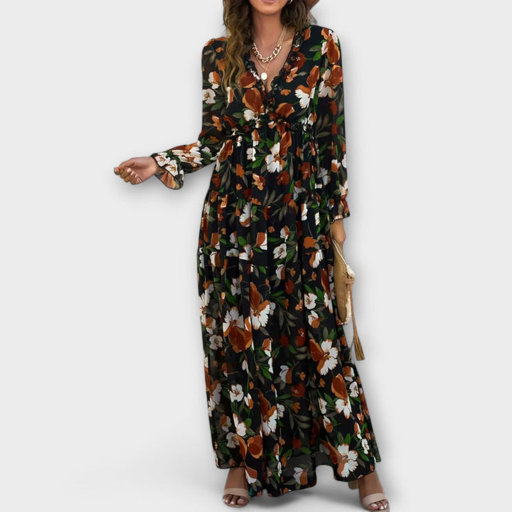 Dark floral maxi dress with v-neck and long sleeves, accessorized with a bag, in a studio setting.